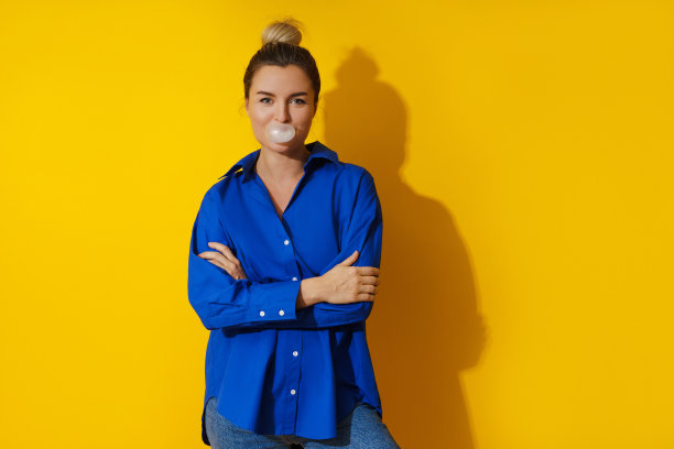 快乐的女人在黄色的背景下用口香糖吹泡泡图片下载