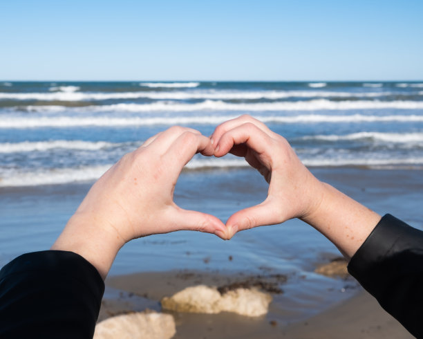 在一个明亮的冬日早晨，中年白人妇女的手在海面上画了一个心形。水平组合。Denia，阿利坎特省。图片下载