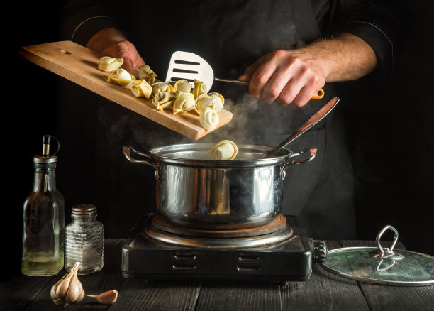 厨师在餐厅厨房里用平底锅准备意大利饺子。特写的厨师手，而工作图片下载