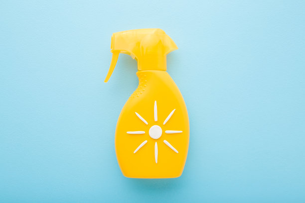 浅蓝色的桌子背景上有黄色的防晒喷雾瓶。柔和的颜色。由白色奶油创建的太阳形状。夏季身体皮肤保护。特写镜头。自顶向下视图。图片下载