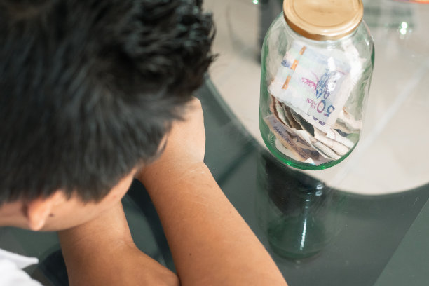 小男孩看着玻璃桌上一个透明的玻璃罐里的存款图片下载