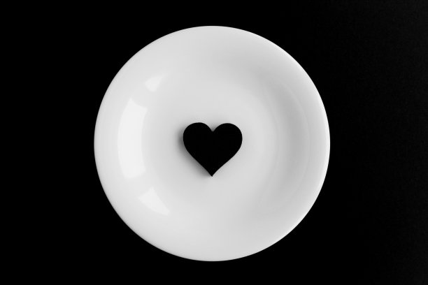 黑色背景上白色盘子上的黑色心形。前视图。特写镜头。图片下载