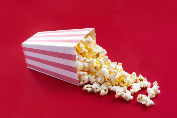 美味的奶酪爆米花从粉色条纹纸盒桶里掉出来，孤立在红色背景上图片下载