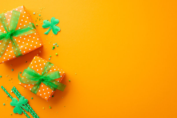 圣帕特里克节的概念。顶部视图照片的礼盒与绿色丝带蝴蝶结洒三叶草和稻草孤立的橙色背景与复制空间图片下载