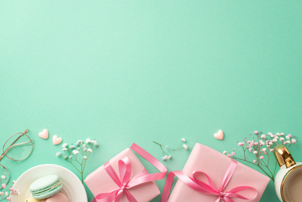 春天的概念。顶部视图照片粉红色礼盒与蝴蝶结茶托与蛋白杏仁饼杯热饮时尚的玻璃杯小心脏和吉思莲花在孤立的蓝绿色背景与空白空间图片下载