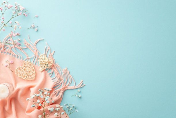 你好，春天概念。顶部视图照片两个藤心小蜡烛在玻璃吉卜草花和粉红色围巾上孤立的浅蓝色背景与复印空间图片下载