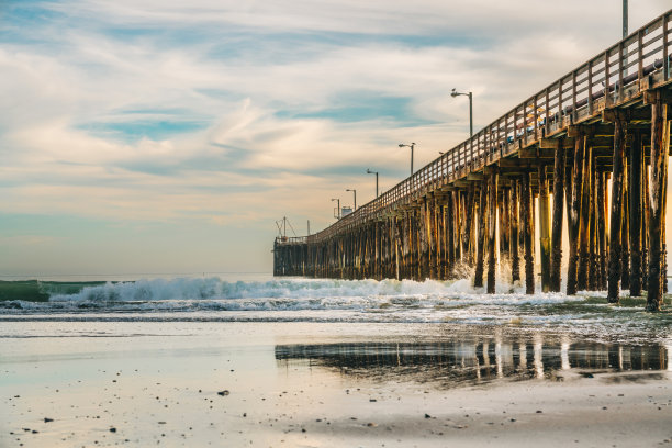 夕阳下长长的木制乡村码头。美丽的太平洋，背景是美丽的多云天空，加利福尼亚的阿维拉海滩图片下载
