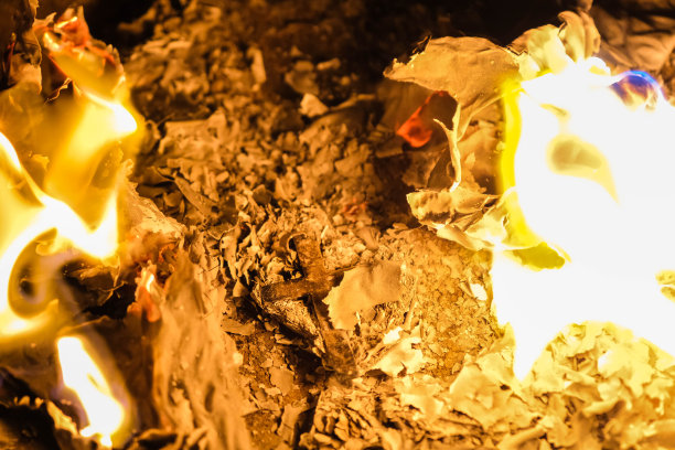 银色十字架上的火焰在夜色中熊熊燃烧。靠近燃烧的纸与银十字架放置在黑色背景的中心。图片下载