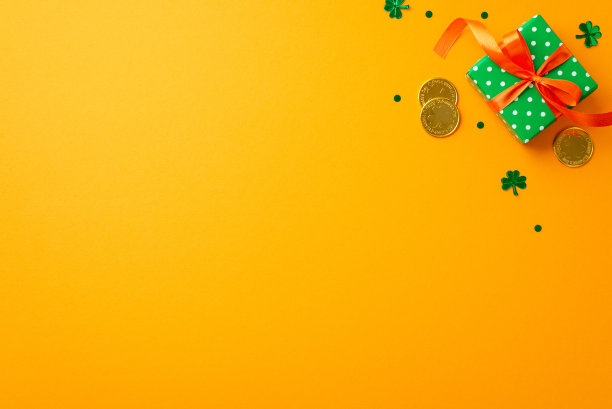 圣帕特里克节的概念。顶部视图照片的小绿色礼品盒与橙色丝带蝴蝶结金币和三叶草形状的纸屑孤立的黄色背景与复制空间图片下载