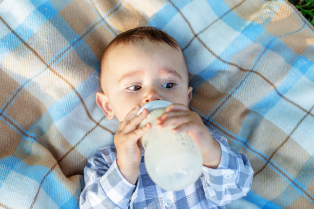 可爱的宝宝躺在毯子上喝奶瓶里的牛奶。婴儿营养图片下载