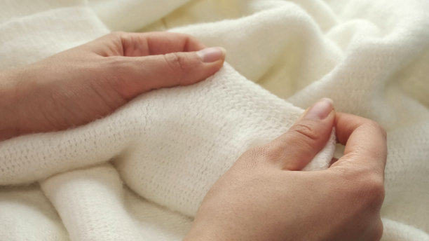 女性的手放在白色长毛绒布料上，有柔软的绒毛。服装行业概念，慢动作。女人在检查衣服的质量时，喜欢布料柔软宜人的质地图片下载