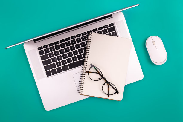 笔记本电脑和空白记事本在绿色背景，俯视图，复制空间。图片下载