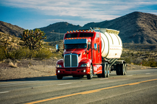 在美国西南部的一个令人惊叹的日落下，明亮的红色半卡车在两车道高速公路上超速行驶，背景是汽车图片下载