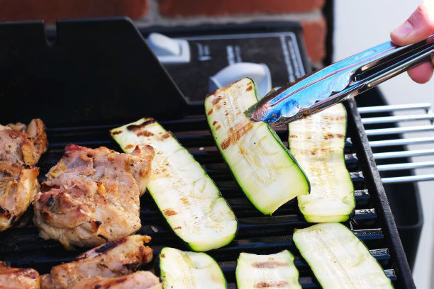 手拿一块烤肉，而烤鸡和祖基尼蔬菜在户外烧烤架近距离照片。食物背景纹理。周末，野餐或派对的概念图片下载