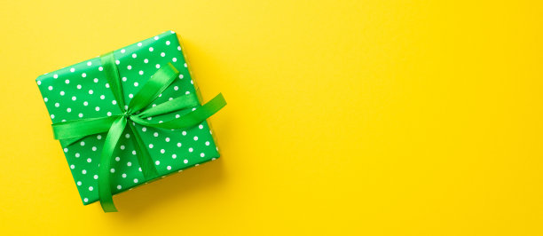 圣帕特里克节的概念。俯视图照片的绿色礼盒包装与波点图案和缎带蝴蝶结孤立的黄色背景与复制空间图片下载