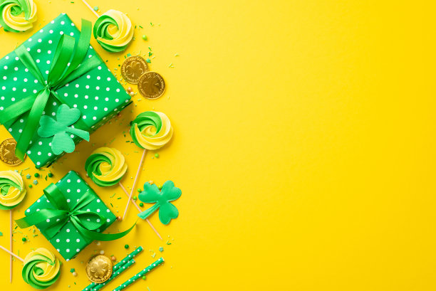 圣帕特里克节的概念。顶部视图照片的绿色礼盒带蝴蝶结蛋白糖洒金色糖果吸管和三叶草孤立的生动的黄色背景与空白图片下载