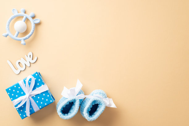 婴儿送礼会的概念。俯视图照片蓝色礼品盒与蝴蝶结铭文爱针织鞋和牙刷玩具在孤立的粉彩米色背景与空白图片下载