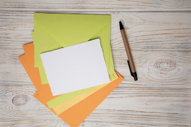 浅绿色，橙色，黄色信封和白色卡片文字在白色木制背景。写信工具图片下载