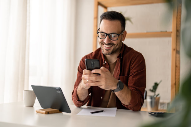 快乐微笑的商人坐在办公桌前，用手机打字图片下载