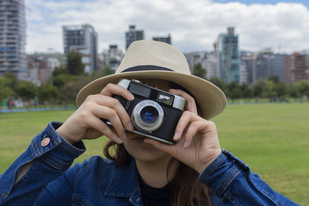 一个戴着棕色帽子和蓝色牛仔裤的女孩用相机拍照的特写镜头图片下载