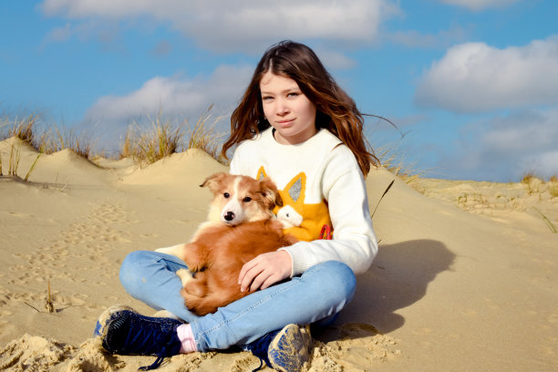 在法国西南部的海滩上，一个漂亮的年轻女孩抱着她的小边境牧羊犬图片下载