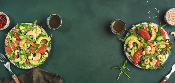 健康新鲜的沙拉配虾仁、鳄梨、葡萄柚、芝麻菜和腰果。表设置。绿色厨房桌子背景，顶部查看横幅图片下载