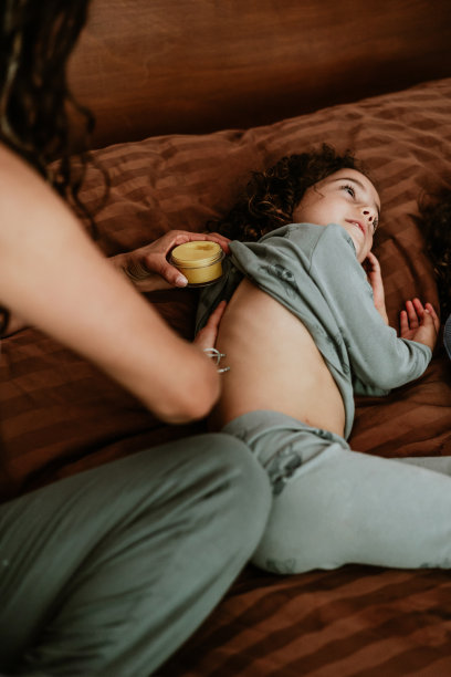 拉丁美洲的墨西哥，一位母亲在儿子的床上给他涂面霜、软膏或香脂图片下载