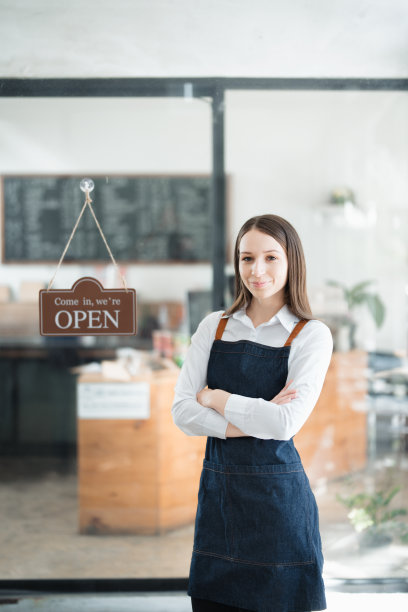 在咖啡店吧台前，一名年轻的亚裔女性正在创业，她系着围裙，露出笑容。企业主，餐厅，咖啡师，咖啡馆，网上中小企业图片下载