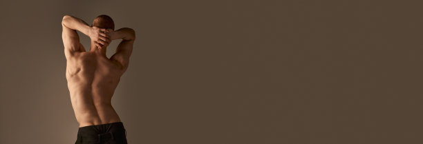 背视照片的赤膊的年轻人在灰色的工作室背景裤子。强壮，放松，肌肉发达的身体，背部。男性的健康、美容和运动生活方式图片下载