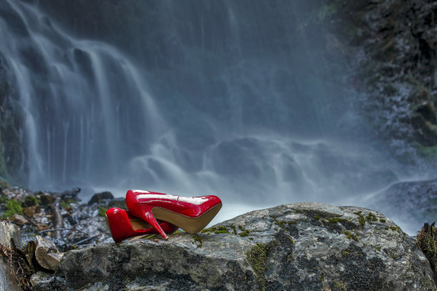 一双红色高跟鞋踩在黑森林瀑布边的岩石上图片下载