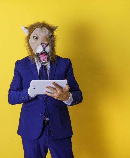 戴着狮子面具的面目全非的商人在用平板电脑。图片下载