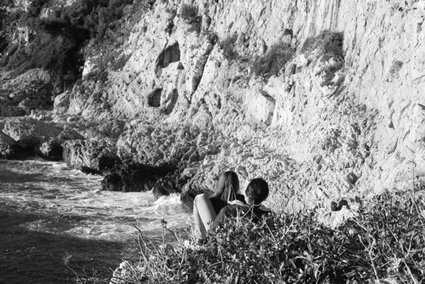 在一个阳光明媚的日子里，一对情侣坐在被悬崖和大海包围的海岸上图片下载