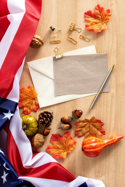 一张木桌的俯视图，上面有感恩节装饰品、美国国旗、信封和一支笔图片下载