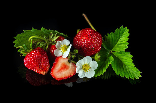 成熟的红色草莓，黑色背景上有叶子和花朵。夏日甜蜜饮食，健康维他命包图片下载