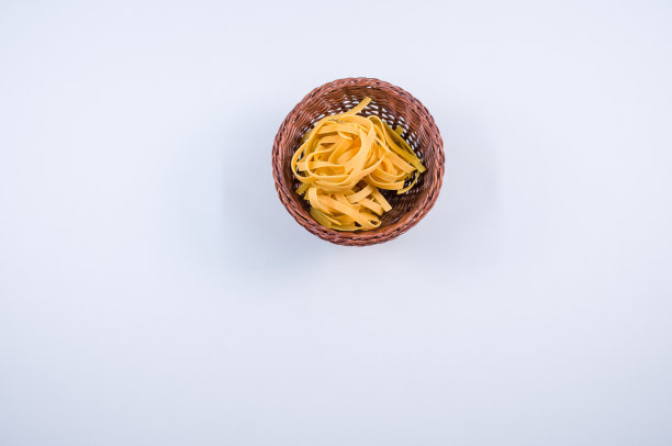 俯视图的棕色柳条碗生鸡蛋面条和筷子孤立在蓝色背景图片下载