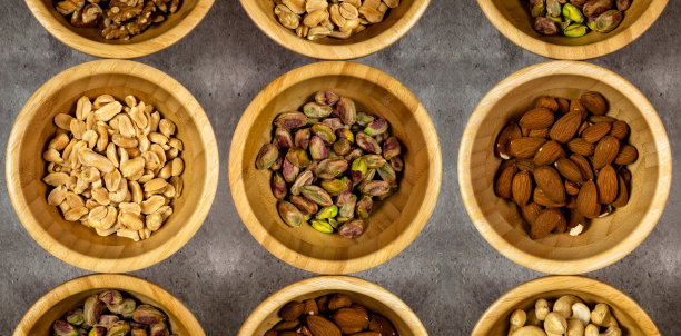 不同种类的干果装在木碗里。花生、杏仁和开心果。俯视图，连续照片。图片下载
