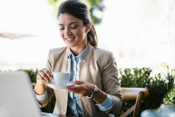 年轻的微笑优雅的女人在西装享受新鲜的咖啡。图片下载