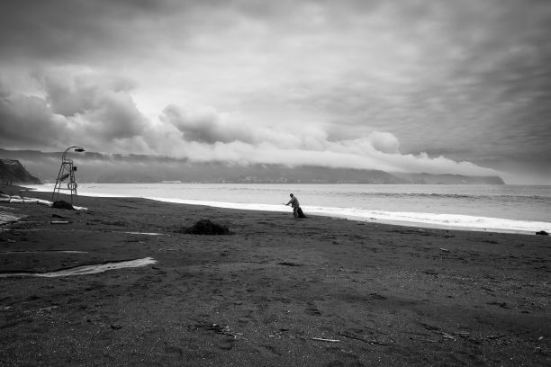 一个渔夫在暴风雨的云层下在沙滩上推网的灰度镜头图片下载