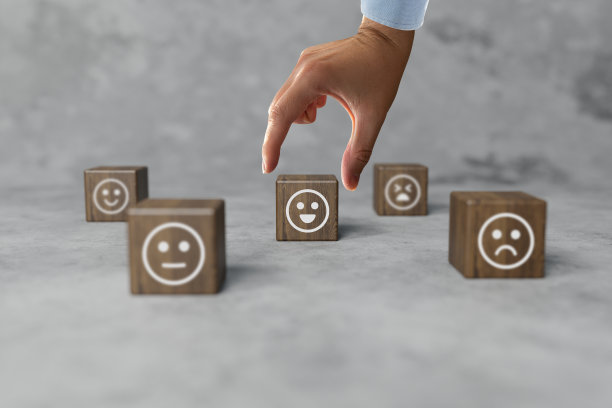木块上有从高兴到悲伤的面孔图标，一只手拿起一个有图标的圆盘。图片下载