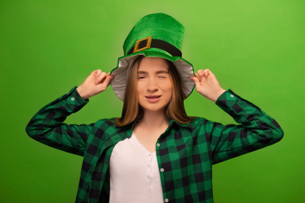 眨眼的年轻女子穿着小精灵帽子和绿色格子衬衫与白色衬衫隔离在彩色绿色背景。

圣帕特里克节庆祝和假日概念。图片下载