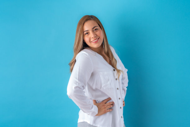 美丽迷人的年轻女商人摆着快乐的姿势，在白色衬衫和灰色裤子。在蓝色背景上隔离。图片下载