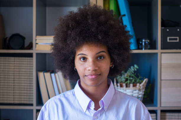 有吸引力的黑皮肤年轻女子的特写肖像与卷曲的非洲发型。非裔美国女商人在办公室工作场所。年轻自信的女士看着相机图片下载