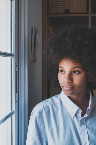 严肃的非裔美国女商人，透过办公室窗户往外看，在思考。一头卷发的女主管在沉思，想办法解决她的问题。职场贴心女士图片下载