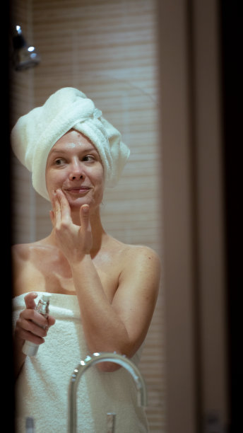 垂直照片，女子在浴室的镜子前涂抹滋养面膜，护肤例行公事图片下载