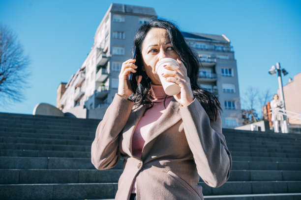 一位女高管在去办公室的路上一边喝咖啡一边和同事们打手机。图片下载