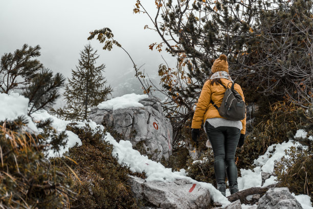 一名白人女性徒步旅行者穿着冬装，背着背包走在森林里的雪道上图片下载
