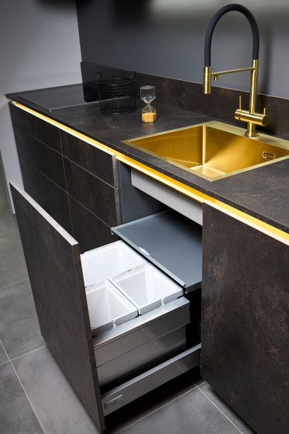 厨余垃圾收纳柜。拉出垃圾箱的厨房抽屉单独废物收集下金色水槽盆和水龙头黑色玻璃电动滚刀石器台面当代平面设计。图片下载