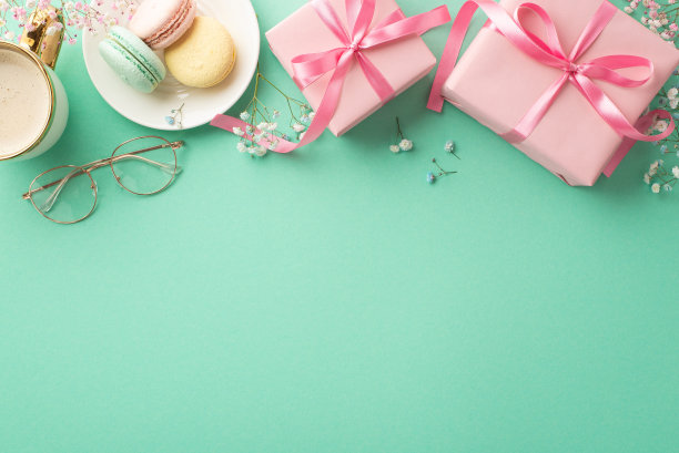春季礼物概念。顶部视图照片粉红色的礼品盒与蝴蝶结盘与马卡龙杯咖啡杯和gypsophila花在孤立的蓝绿色背景与复制空间图片下载