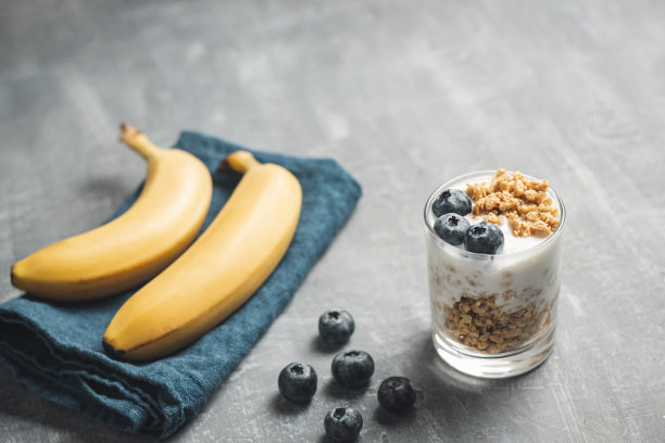 格兰诺拉麦片麦片配白色酸奶、蓝莓和香蕉水果，放在蓝色餐巾上，灰色背景的杯子里图片下载