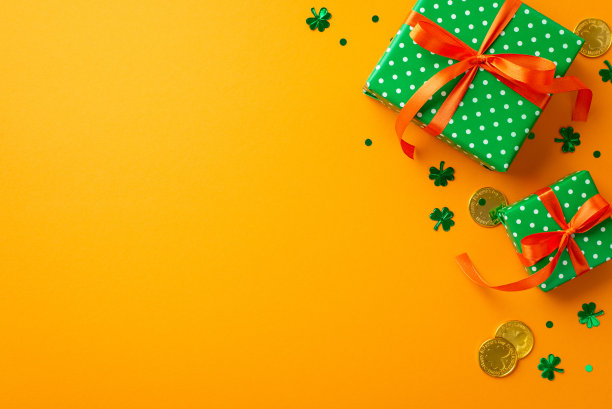 圣帕特里克节的概念。顶部视图照片的绿色礼品盒与橙色丝带蝴蝶结金币和三叶草形状的五彩纸屑孤立的黄色背景与空白图片下载